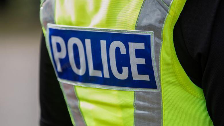 A police officer wearing a high vis jacket. The jacket says "POLICE".