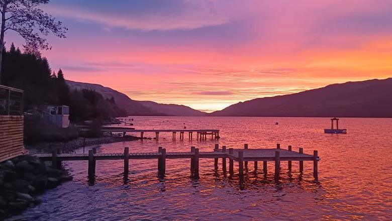 Two wooden jettys jut up into the loch which is purple from the sunrise.