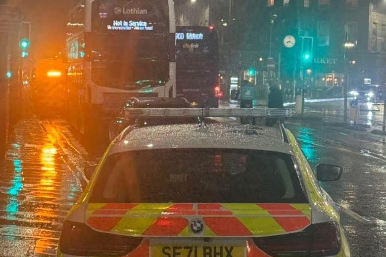A police car is in the foreground. In the background is the back of the bus that was involved in the incident.