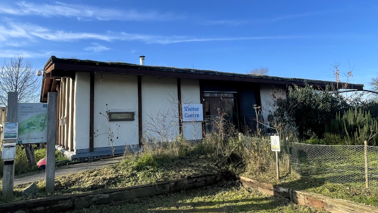 The Romney Marsh Visitor Centre, with white walls and a dark brown roof and wall beams, with vegetation in front of the building and a blue sky behind it.