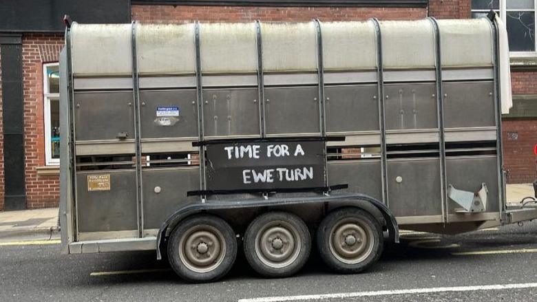 A trailer on a car saying "Time for a Ewe-turn"