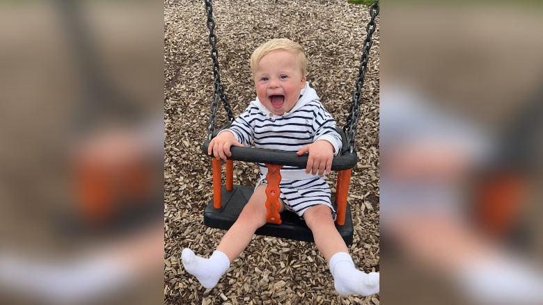 AJ, a blonde toddler with Down's Syndrome, laughs while on a swing