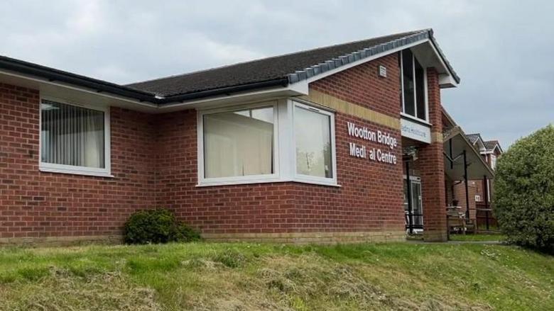 A modern-looking brick building with large white-framed windows and a sloping roof. The large sign on the front reads Wootton Bridge Medical Centre