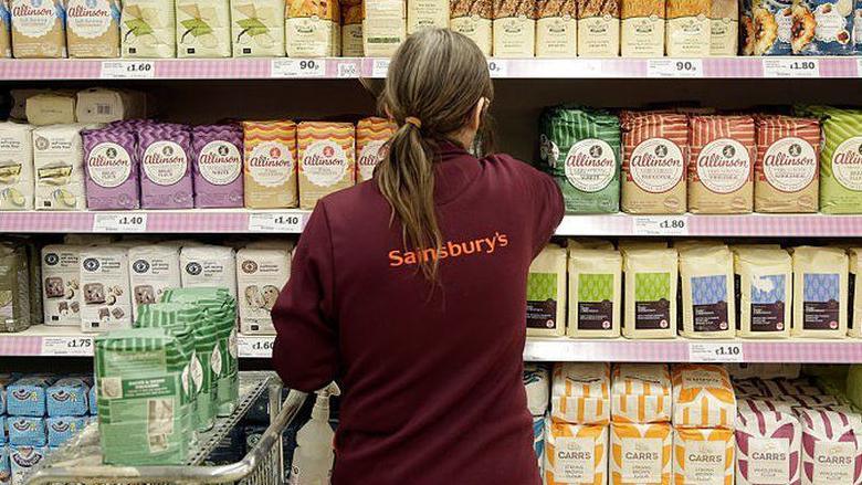 A supermarket shop worker stacks shelves with flower, on the back of her uniform the Saisnbury's log can be seen