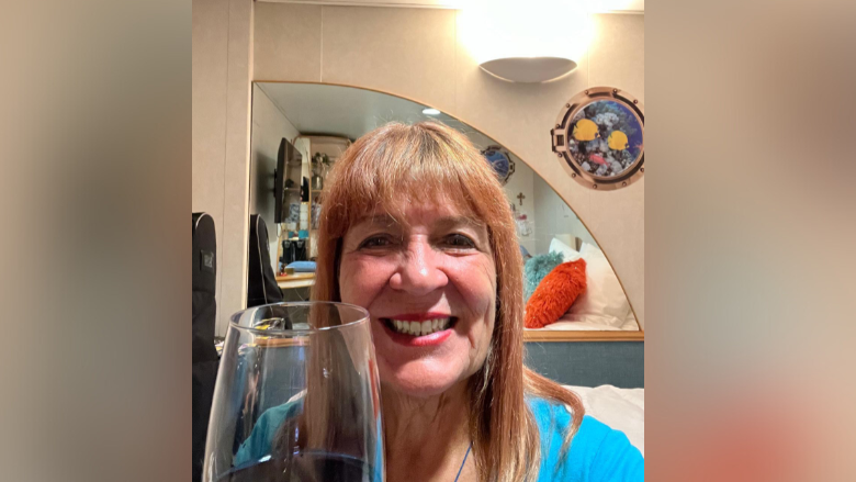 Woman smiles as she holds glass of red wine in cabin.