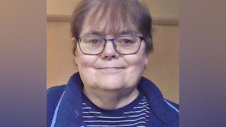 Fiona Brown is wearing glasses. She has a blue fleece-type top over a blue and white striped t-shirt.