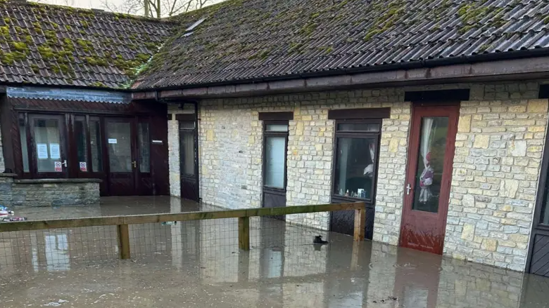 A flooded walkway outside a pale brick building with a brown roof.