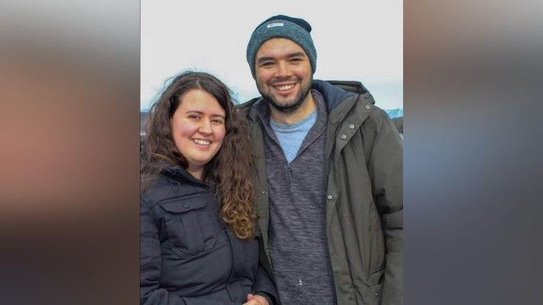 Georgia Tate and Andrew Lartey smiling at the camera outside. Georgia has long brown curly hair and Andrew has a dark beard and is wearing a beanie.