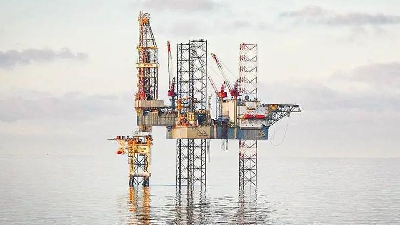 A picture of an installation in the North Sea, it's metal legs are in the water, under a grey sky.
