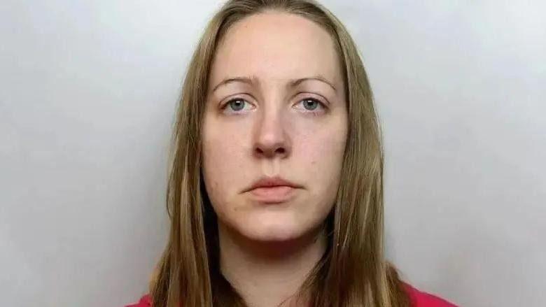 A mugshot of Lucy Letby with dark blonde hair past her shoulders, blue/grey eyes and a red top on.
