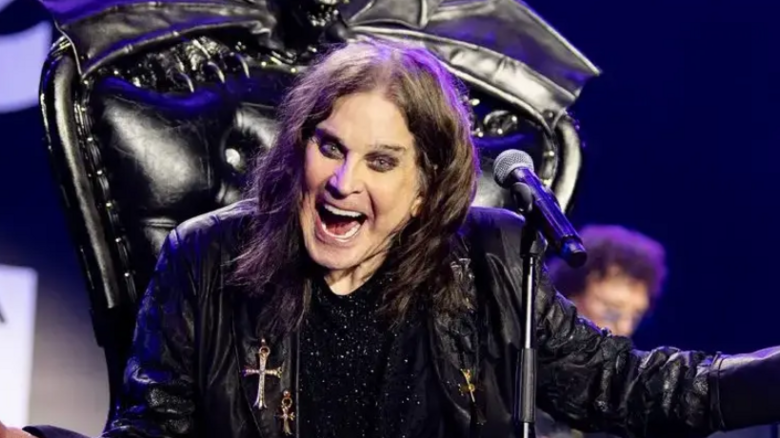 Ozzy Osbourne, dressed in a black leather jacked sat on a black throne with a microphone in front of him