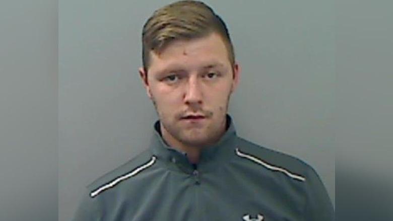 A mugshot of Jake Wray who has brown, short hair. He's wearing a grey tracksuit top.