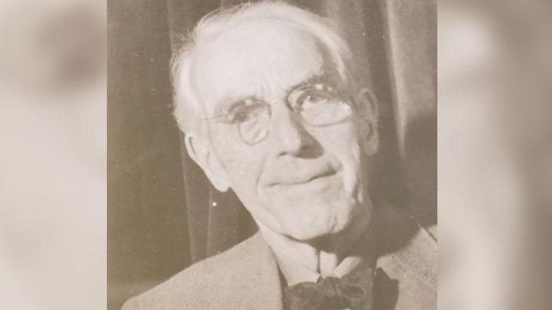 Photographer Henry Wykes who documented Exeter's history is photographed aged 87. He is wearing a suit jacket with a bow tie and glasses in this head and shoulders shot and is smiling at the camera.