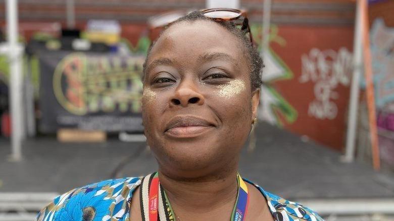 LaToyah McAllister-Jones smiles at the camera. She has gold glitter on her cheekbones and is wearing brown sunglasses on top of her head.