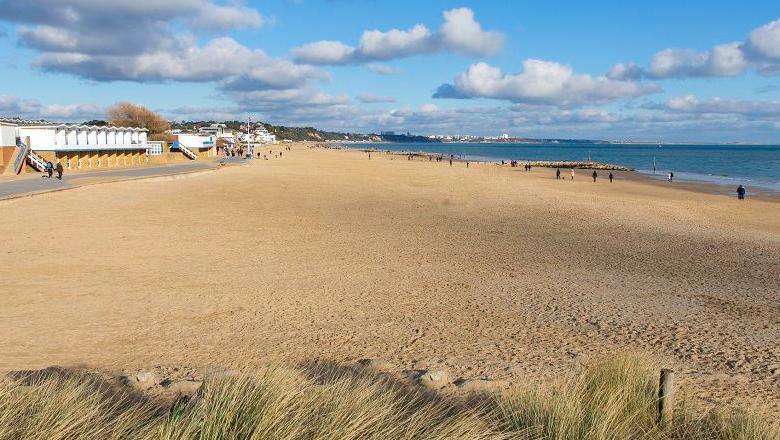 Sandbanks beach with light coloured sand and blue sea. White buildings and people can be seen in the background