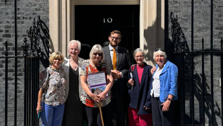 Freddie van Mierlo in a grey suit, blue shirt and orange tie, along with five women all with grey hair.