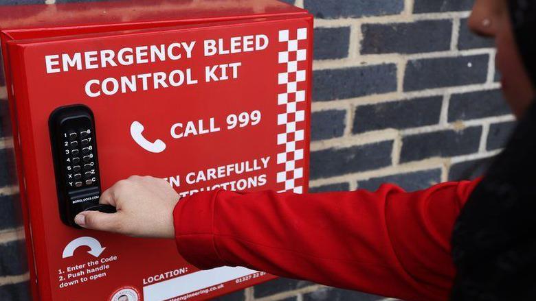 A woman trying to access the Cowley bleed kit. She is wearing a red long-sleeve top. He face is visible only in profile and she is wearing a black hijab.