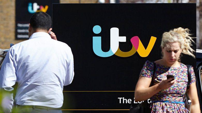 Two people walk outside the ITV studio with a big ITV logo in the background.