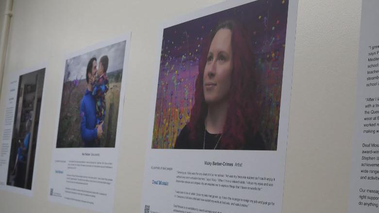 Different people in the exhibition with a different story on a wall of a hospital corridor