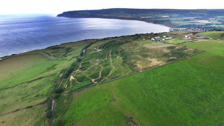 A view of the green field, cliff edge and beach taken on a walk along the Cinder Trail to Robin Hoods Bay from Whitby