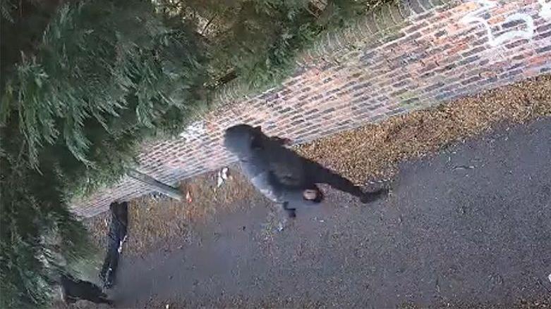 CCTV shows a man, dressed in black, lying unconscious in an alleyway after being attacked. The attackers, both of whom are also dressed in black clothing, can be seen nearby, running from the scene.