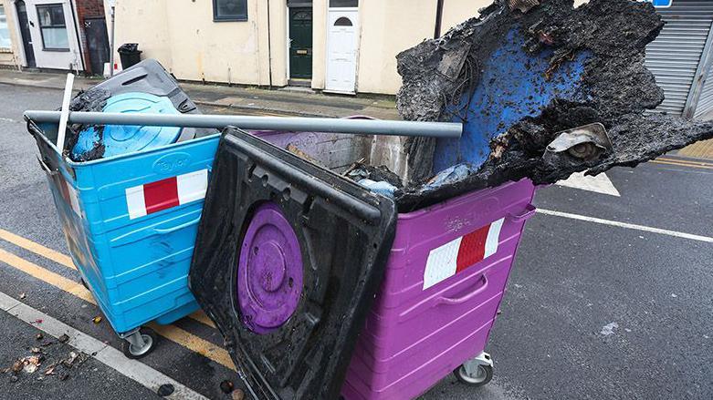 Debris fills charred wheelie bins on County Road