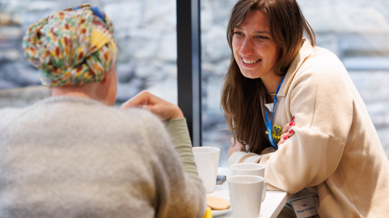 Two women sitting at a table at a pop-up cafe chatting over cups of tea and biscuits