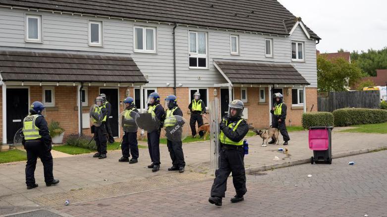 Armed police officers stood outside houses wearing protective gear