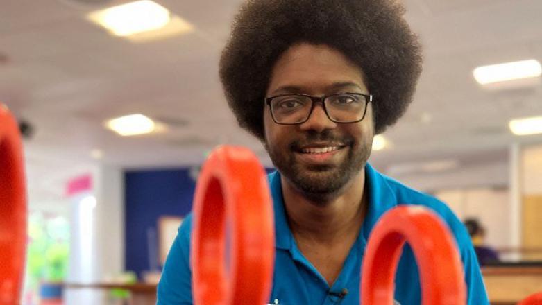 Mario Satchwell wearing a blue polo shirt and dark rimmed glasses looking at camera