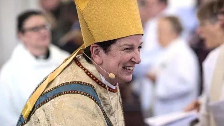 Bishop Anne Dyer, woman smiling, wearing golden-coloured religious clothing 