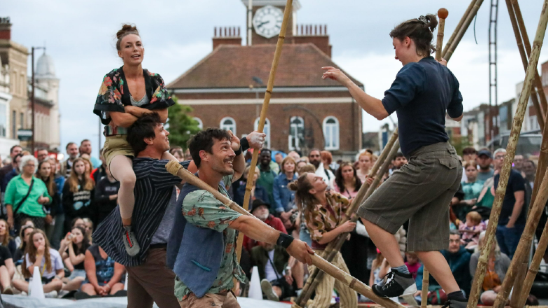 Performers balance on wooden poles in front of a crowd.