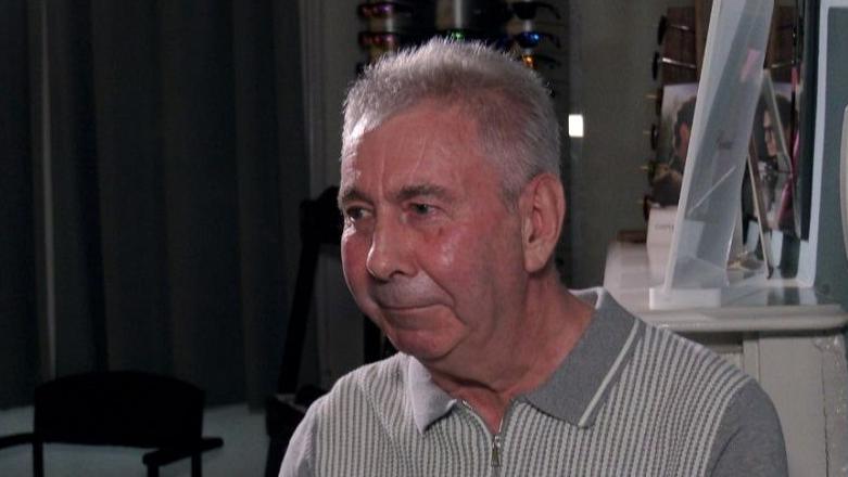 Robert Campbell looking to the side of the camera at the opticians, wearing a grey t-shirt and has grey hair.