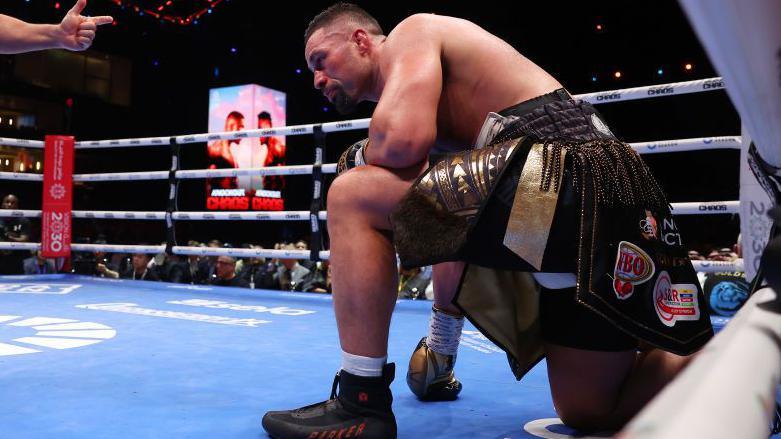 Joseph Parker on one knee, wearing white socks in the ring 