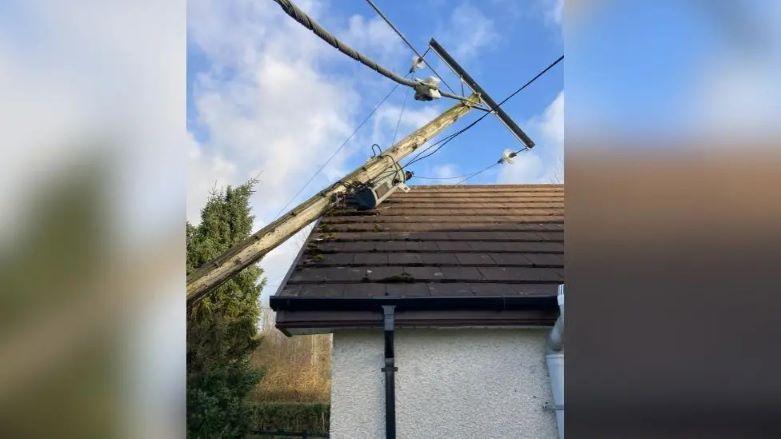 An electrical utility pole has fallen on the roof of a house 