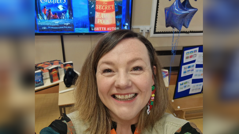 Lisette Auton smiles in front of a display featuring her book covers