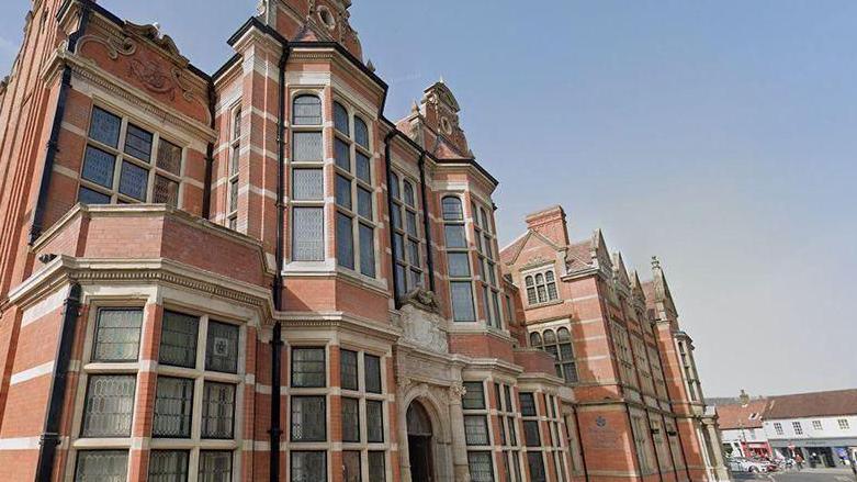 A Google street view image of County Hall in Beverley. The red brick and sandstone building stands in the sunshine with an empty tarmac road alongside.