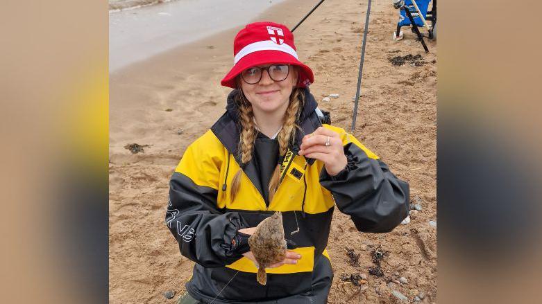 Lexie wearing yellow and black coat while posing with a small turbot fish