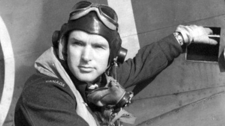 A black and white photo of Lieutenant John Saville in front of a plane. He is wearing his uniform which includes a pilot's cap and goggles. 