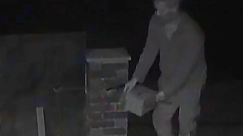 A black and white image shows a man taking a charity poppy box from a wall