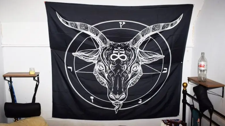 A black piece of material is hanging on a wall with a satanic image in white.