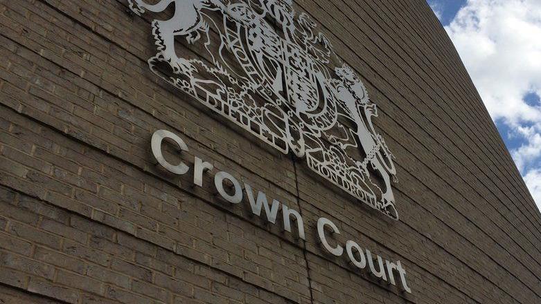 A close up view of the criminal courts crest and the words "crown court" on the Cambridge Crown Court building. It is a light coloured brick building. 