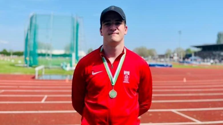 Jack Burgess captured from the waist up, in a red club jumper. He is wearing a medal and smiling towards the camera