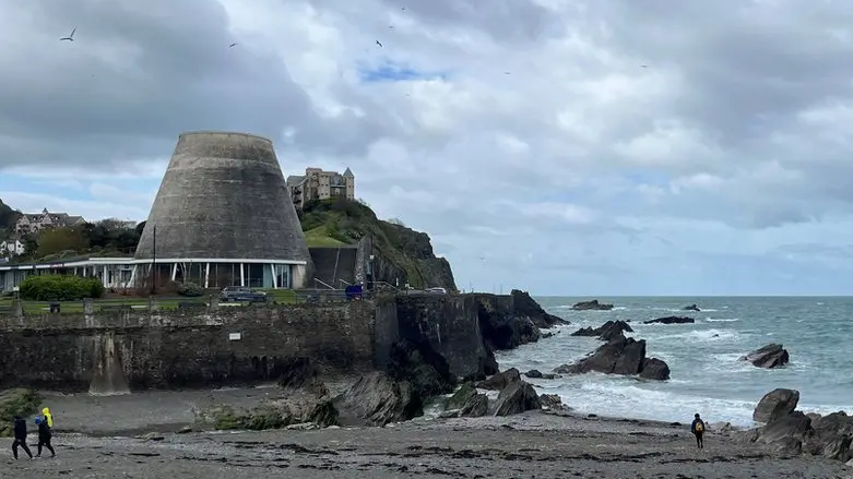 A view of the beach and the sea at Ilfracombe with rocks to the right and the conical tower of the Landmark Theatre on the left