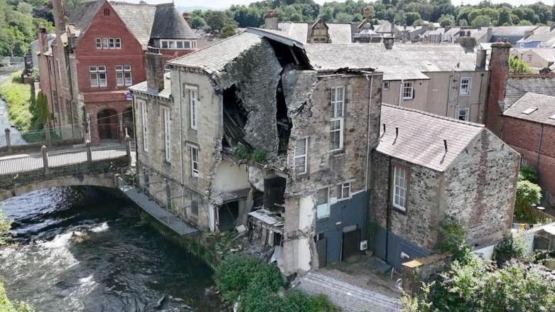 View of the rear of the Old Courthouse. A large section of the stone-built property is missing. It stands next to the River Cocker and Cocker Bridge.