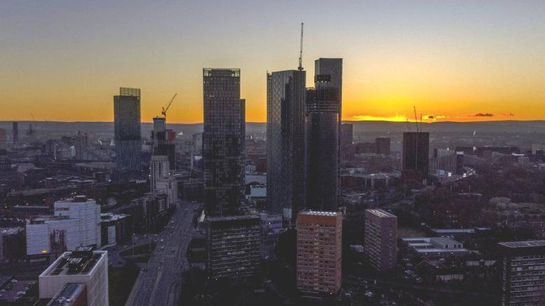 Skyline of Manchester at sunset - skyscrapers are shown towering above the buildings below