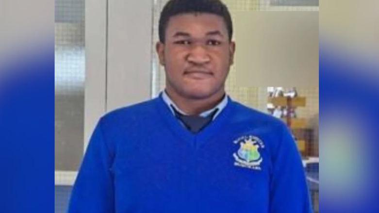 Emmanuel Familola wearing his school uniform. He has short, dark hair and is wearing a bright blue jumper, a light blue shirt and a navy tie.
