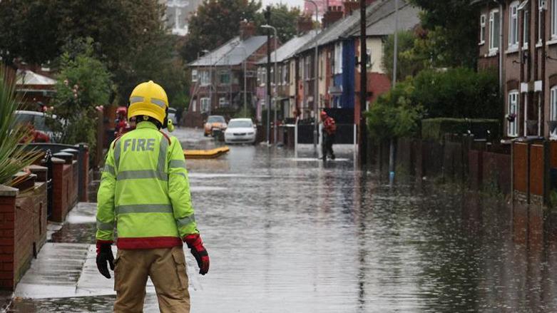 Fire fighter in a road flooded showing a rescue sled in the distance 