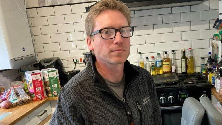 Dan Boatright-Greene in a kitchen with white tiling and food packages on the side