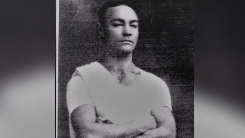 A black and white picture of Sydney Bolesworth with his arms folded. He is wearing a white t shirt.