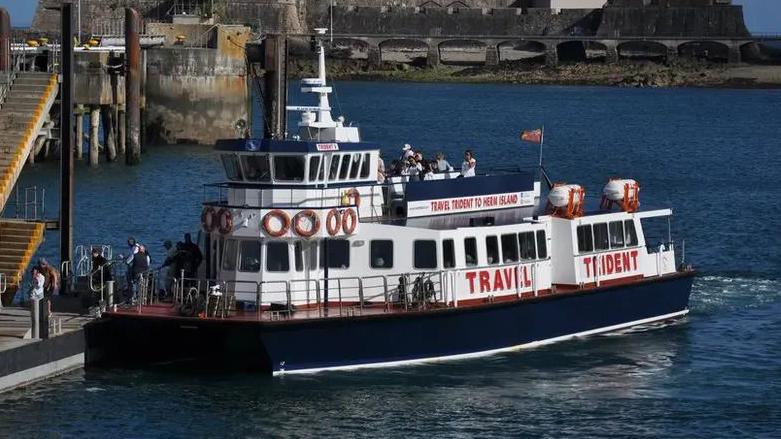 A blue and white boat, with red life rings and writing saying Travel Trident, sits near a dock as passengers get off it.